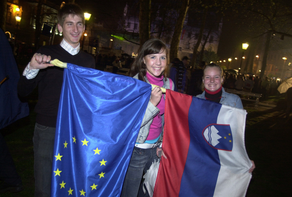 mladi ljudje v rokah držijo slovensko in EU zastavo ter se smejijo