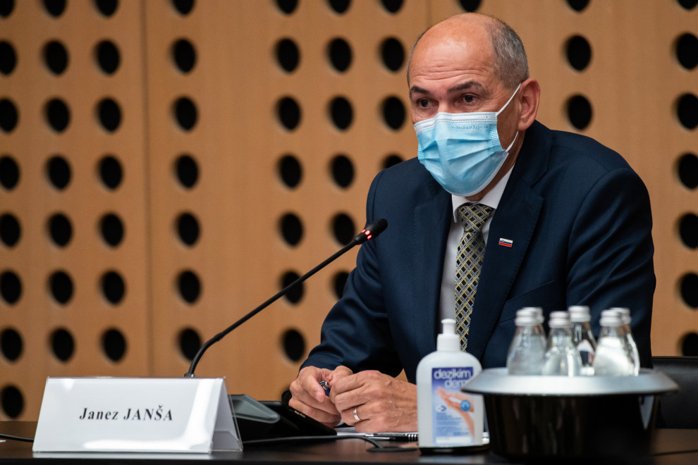 Predsednik vlade Janez Janša sedi za mizo z masko na obrazu, pred njim je mikrofon.