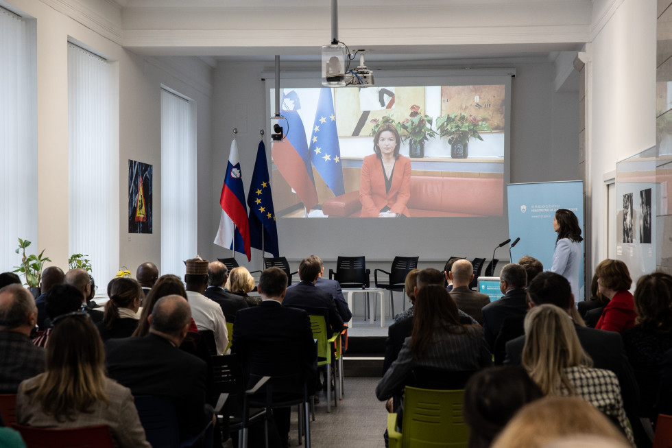 ministrica Fajon na zaslonu, udeleženci poslušajo