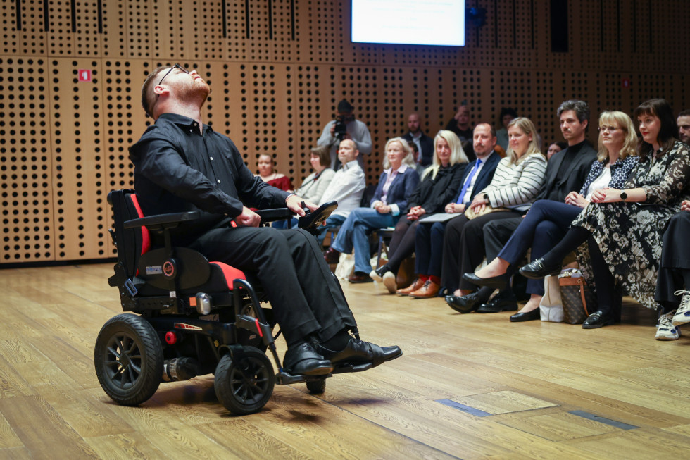 V ospredju moški na invalidskem vozičku med plesno točko, v ozadju sedijo gledalci.
