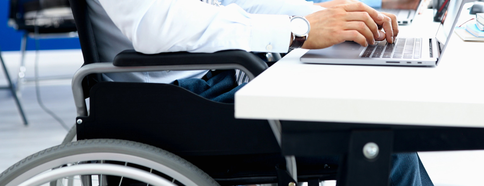 A person in a wheelchair is sitting at a desk and typing on a laptop
