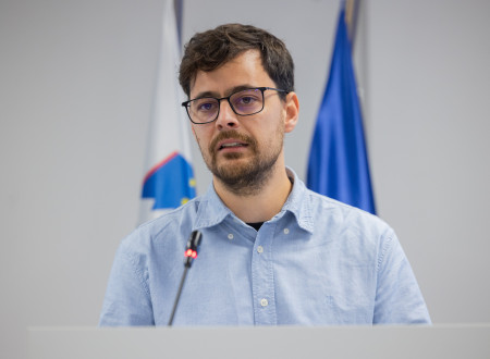 Državni sekretar, pred njim mikrofon, v ozadju zastave