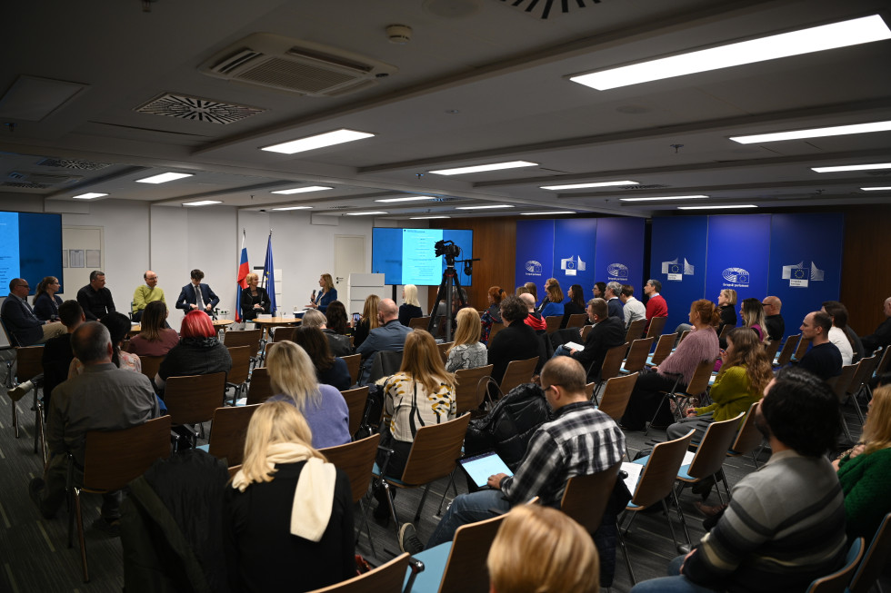 Udeleženci posveta sedijo v dvorani in poslušajo.