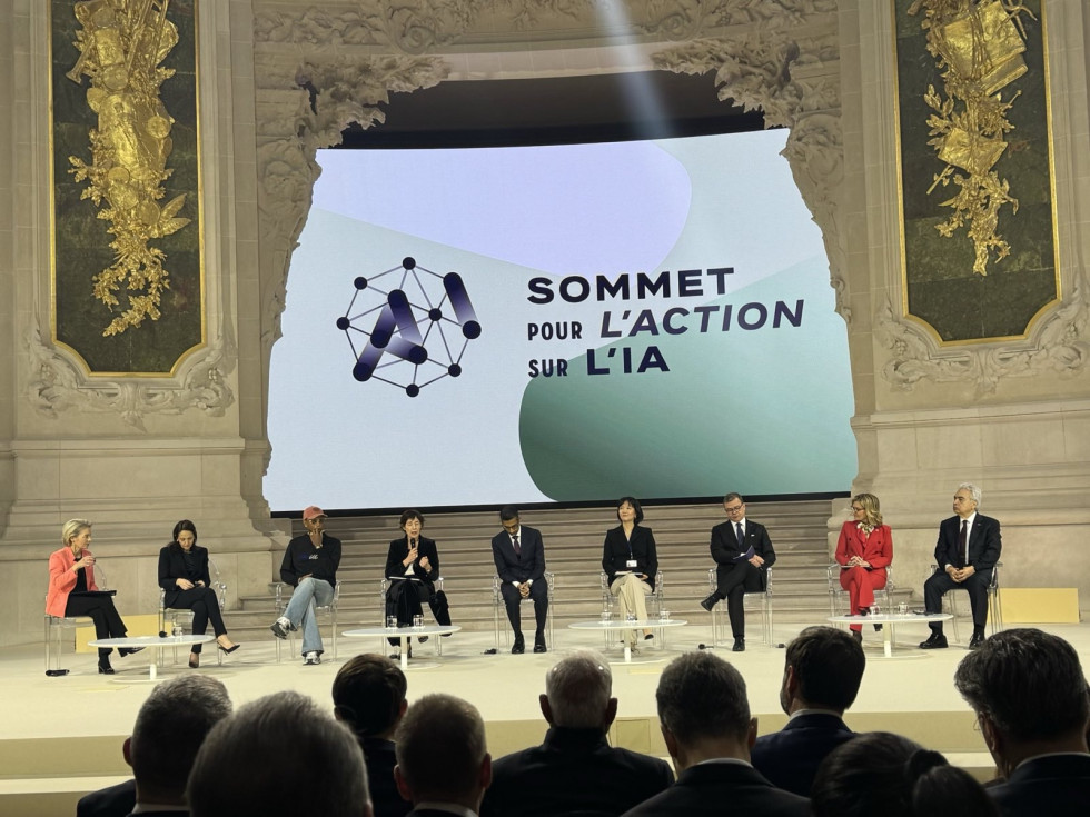 Photograph of a panel. The speakers are seated on stage and addressing the audience while sitting.
