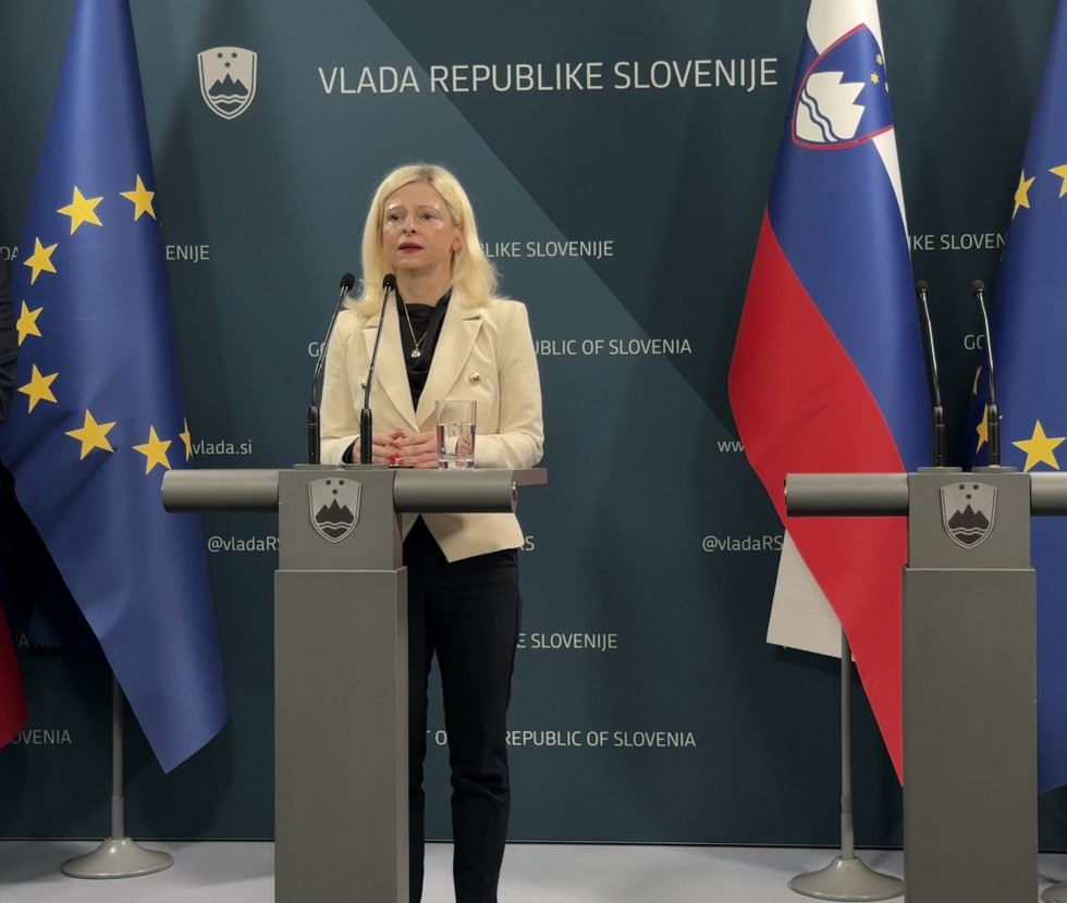 Ministrica stoji za govorniškim odrom. Zadaj slovenska in evropska zastava.