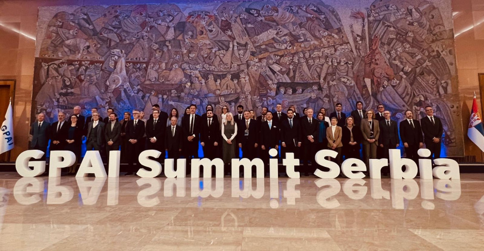 Skupinska fotografija udeležencev zasedanja pred veliko rjavo poslikano steno in za napisom GPAI Summit Serbia