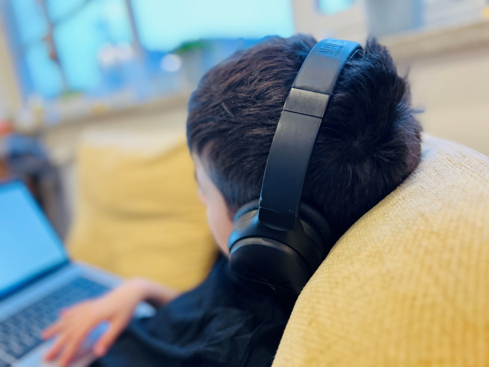 Otrok z naglavnimi slušalkami glede na ekran laptopa.