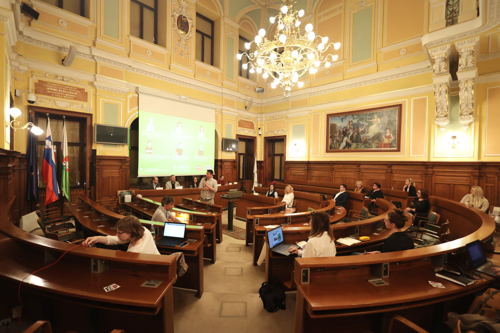 Udeleženci sedijo v dvorani mestnega sveta v Ljubljani.