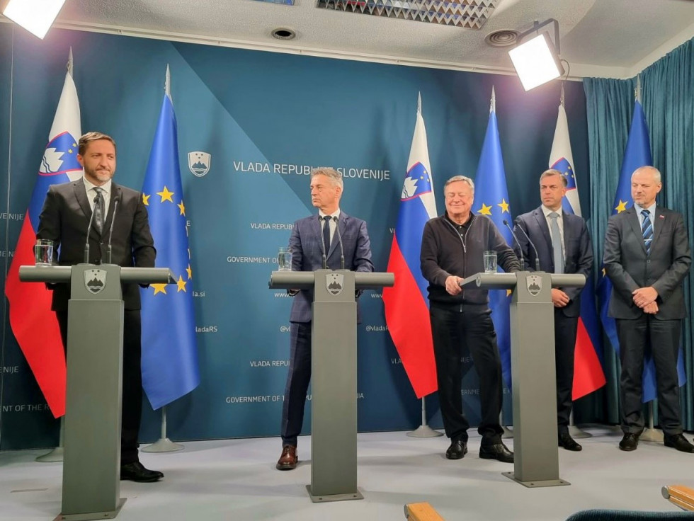 Govorci stojijo za govorniškim pultom in dajejo izjavo za medije, v ozadju sta zastavi Slovenije in Evropske unije