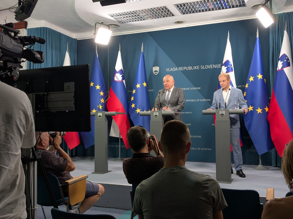 Minister in državni sekretar stojita na odru in govorita, v dvorani
