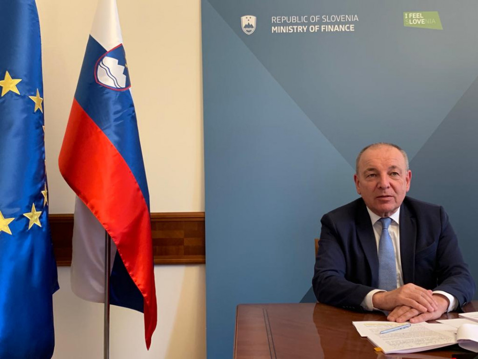 Minister sedi za mizo v svoji pisarni, pred sabo ima delovne papirje, levo od mize stojita slovenska in EU zastava