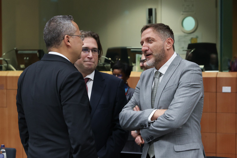 Trije moški v poslovnih oblekah stojijo in se pogovarjajo.