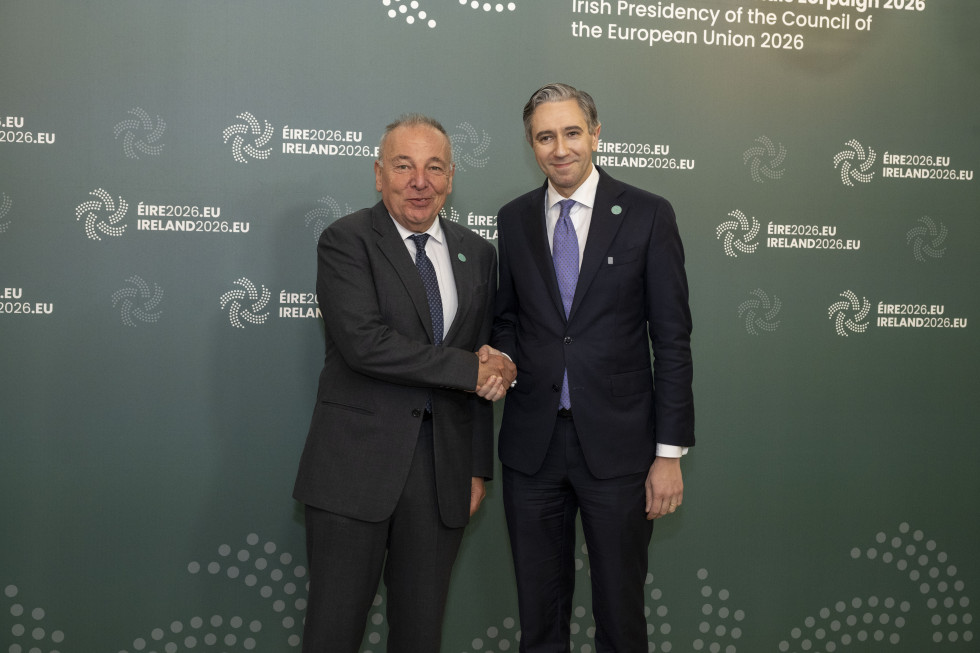 Ministra se rokujeta, za njima velik zelen pano z logom in napisom Ireland2026.eu
