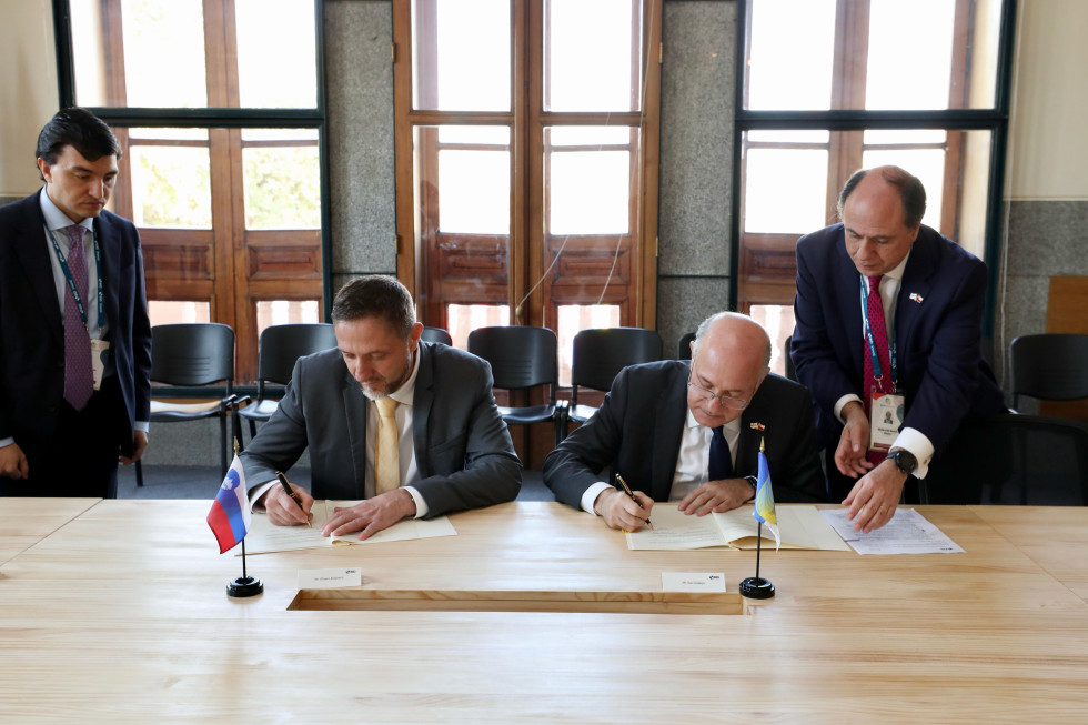 Minister Klemen Boštjančič in predsednik IDB Ilan Goldfajn sedita za mizo in podpisujeta sporazum.