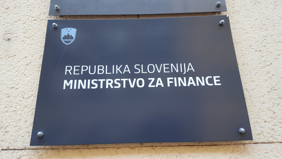 Black signboard of the Ministry of Finance. Top left Slovenian coat of arms in blue, below white inscription Republic of Slovenia, Ministry of Finance.