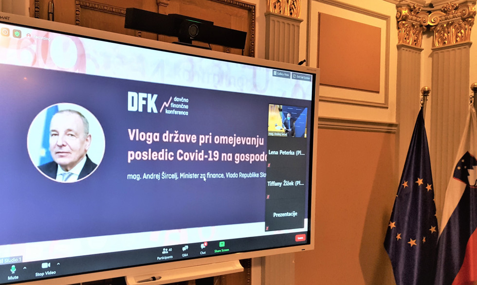 Na platnu projekcija Davčno finančne konference, v zgornjem desnem kotu v videokonferenčnem oknu minister za finance, ki nagovarja udeležence videokonference.  