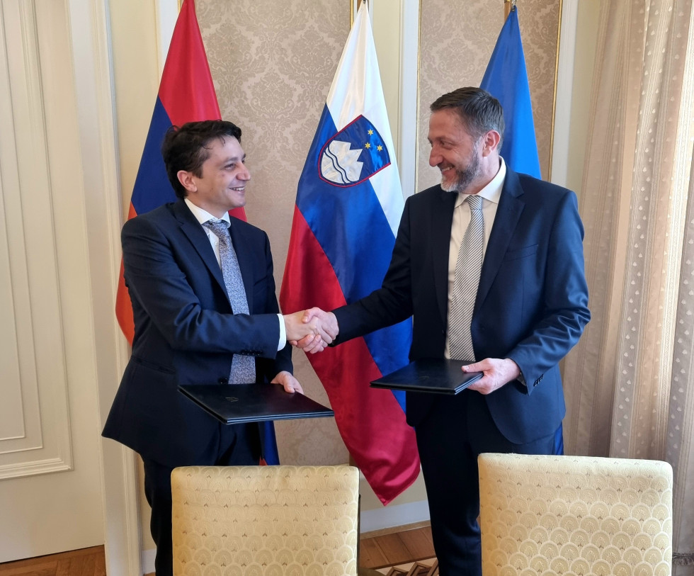 Slovenski in armenski finančni minister stojita pred zastavami, se rokujeta, v drugi roki pa držita podpisan memorandum o sodelovanju.