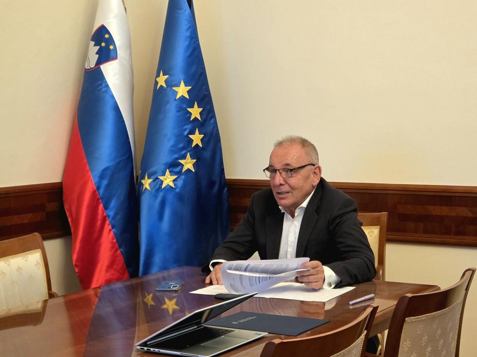 Minister sedi za mizo, v ozadju sta zastavi Slovenije in Evropske unije