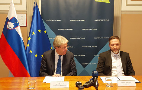 Evropski komisar za gospodarstvo Paolo Gentiloni in minister za finance Klemen Boštjančič (The Commissioner and the Minister are sitting at the table with microphones in front of them. In the background are the flags of Slovenia and the EU and a blue billboard with the sign Ministry of Finance on it.)
