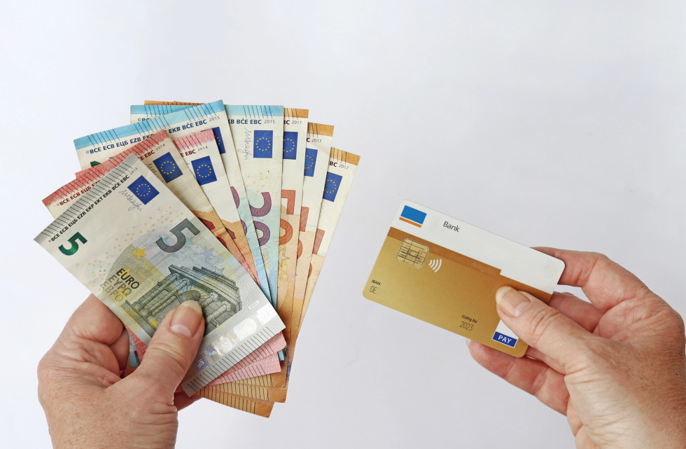 Slika gotovine v eni roki in bančne kartice v drugi roki