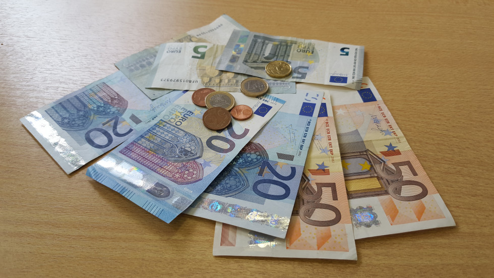 Na mizi razpršeno leži denar v papirnati obliki za 50, 20 in 5 evrov. Na njem, prav tako razpršeno, ležijo kovanci za 1 evro, 20 centov in 5 centov.