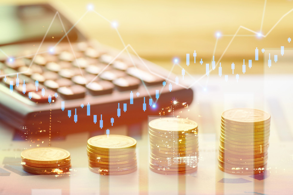 Kalkulator v ozadju, v ospredju več stolpcev kovancev, zloženih po velikosti in graf.