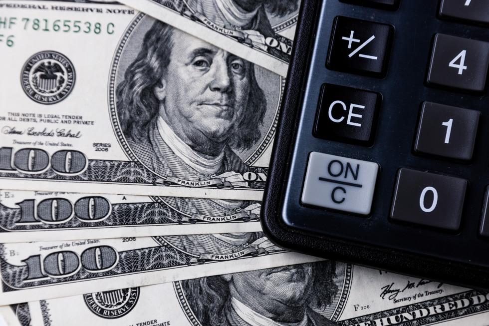 Dolarski bankovci na katere je položen kalkulator, ki se ga na fotografiji vidi le delno. 