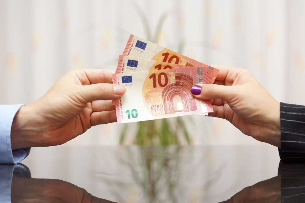 Ženska roka predaja moški roki tri bankovce za deset evrov.