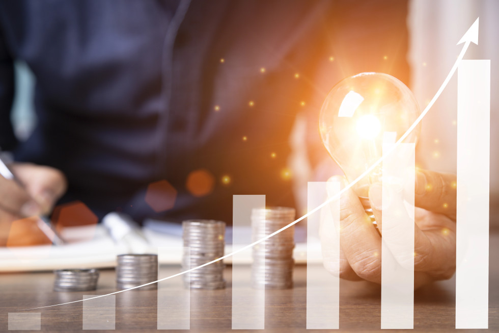 Moški drži žarnico, v ospredju so kovanci zloženi v stolpce, ki naraščajo proti desni.