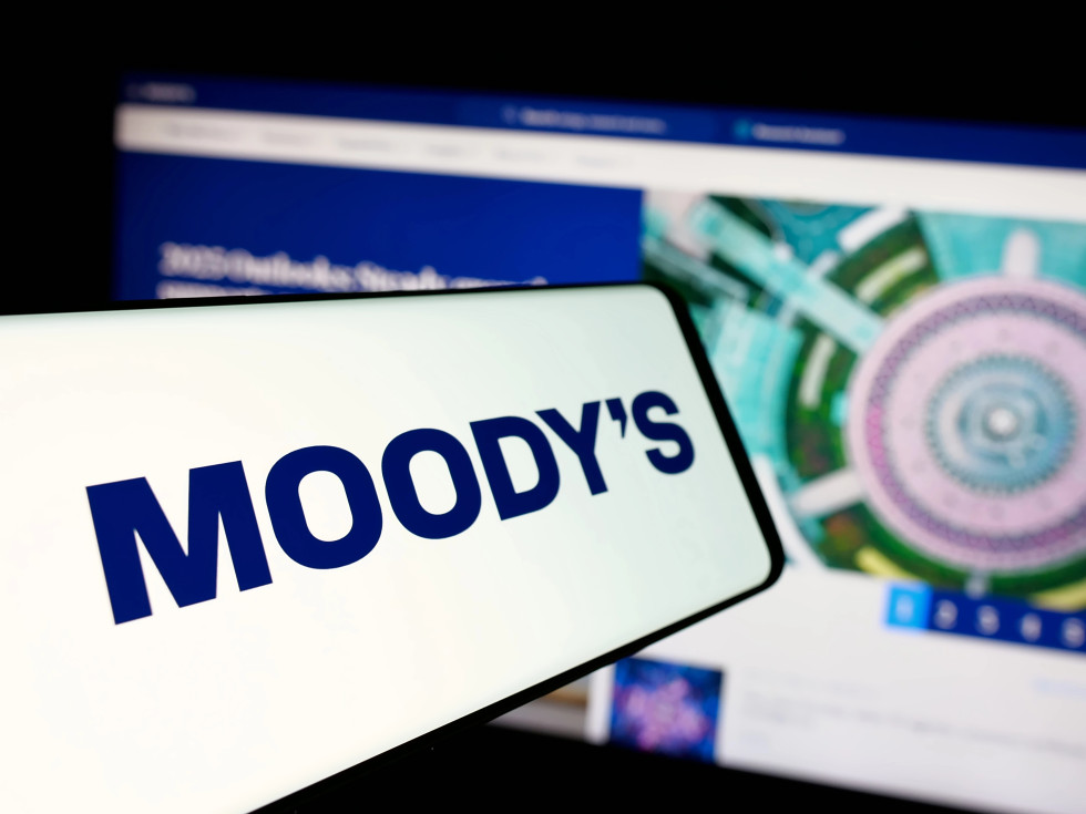Na mobitelu je izpisano ime Moody's, v ozadju je namizni računalnik