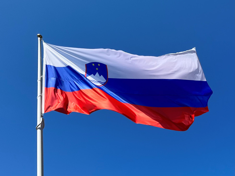 Slovenian flag on a pole, blue sky in the background.