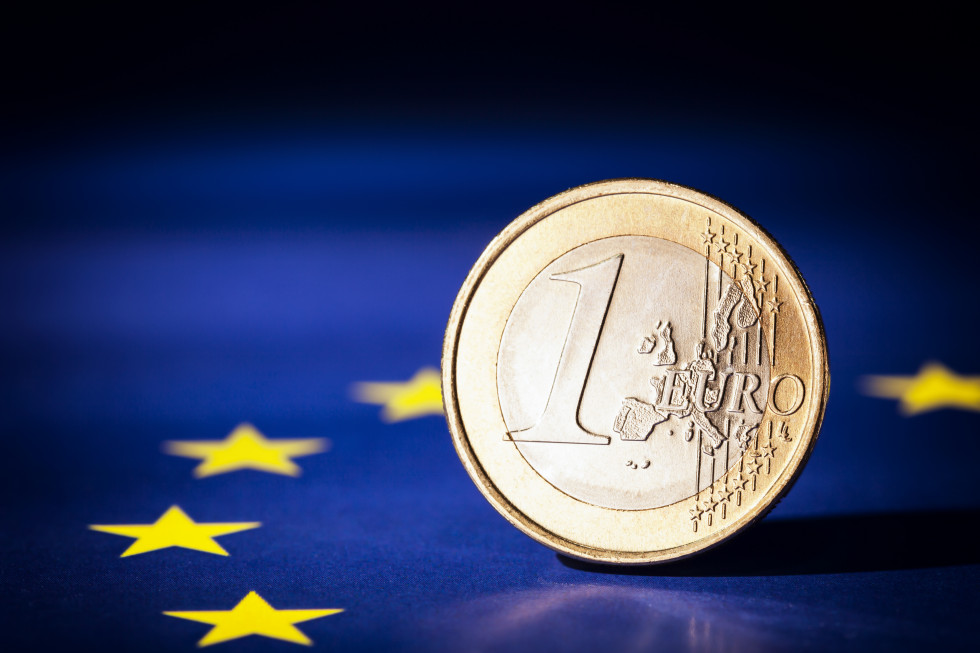 Zastava EU leži, kovanec za en evro pa stoji na njej