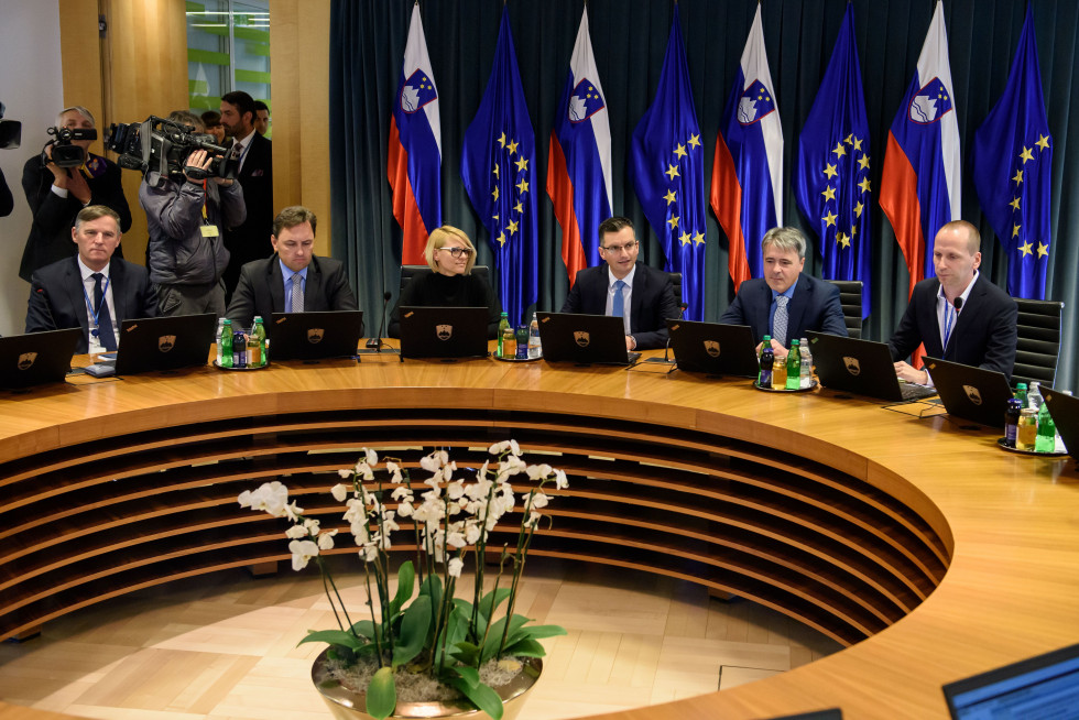 Ministri sedijo za okroglo mizo, za njimi stojijo zastave Slovenije in EU