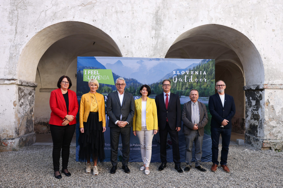 Sedem udeležencev novinarske konference stoji zunaj pred panojem. 
