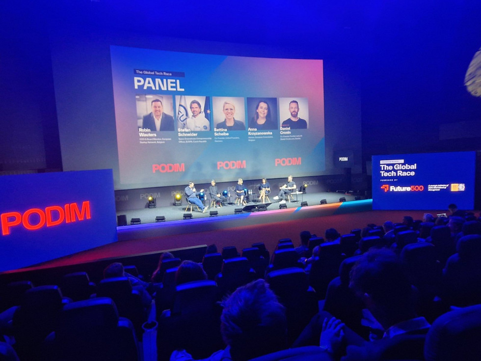 Občinstvo spremlja panelno razpravo na velikem zaslonu v konferenčni dvorani.