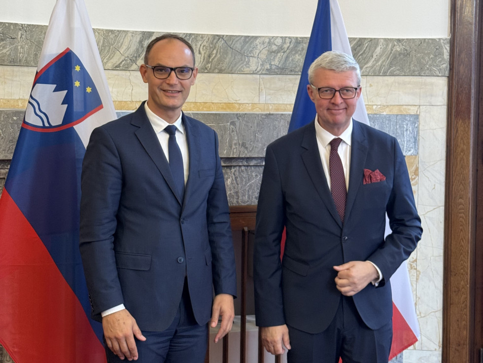 Ministra stojita pred slovensko in češko zastavo. V zaprtem prostoru.