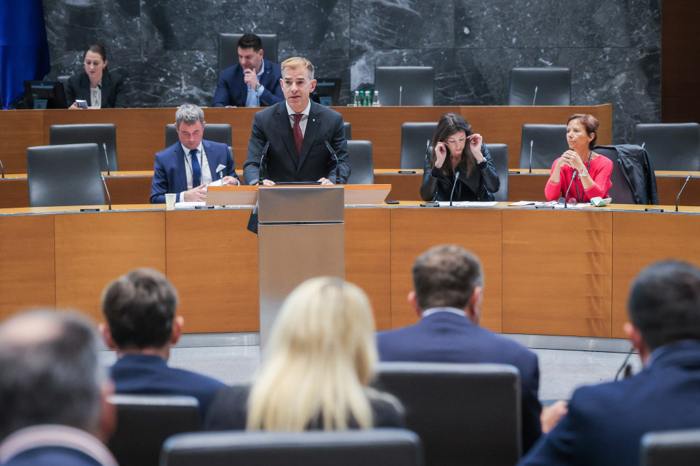 Nagovor državnega sekretarja. Stoji za govornico v dvorani Državnega zbora Republike Slovenije.
