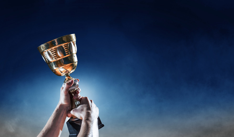 Moški v rokah drži pokal. 