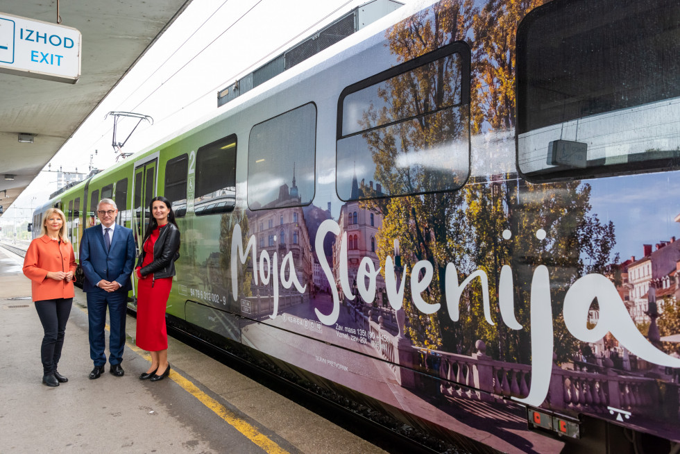 Tri osebe stojijo ob vlaku na katerem je napis Moja Slovenija