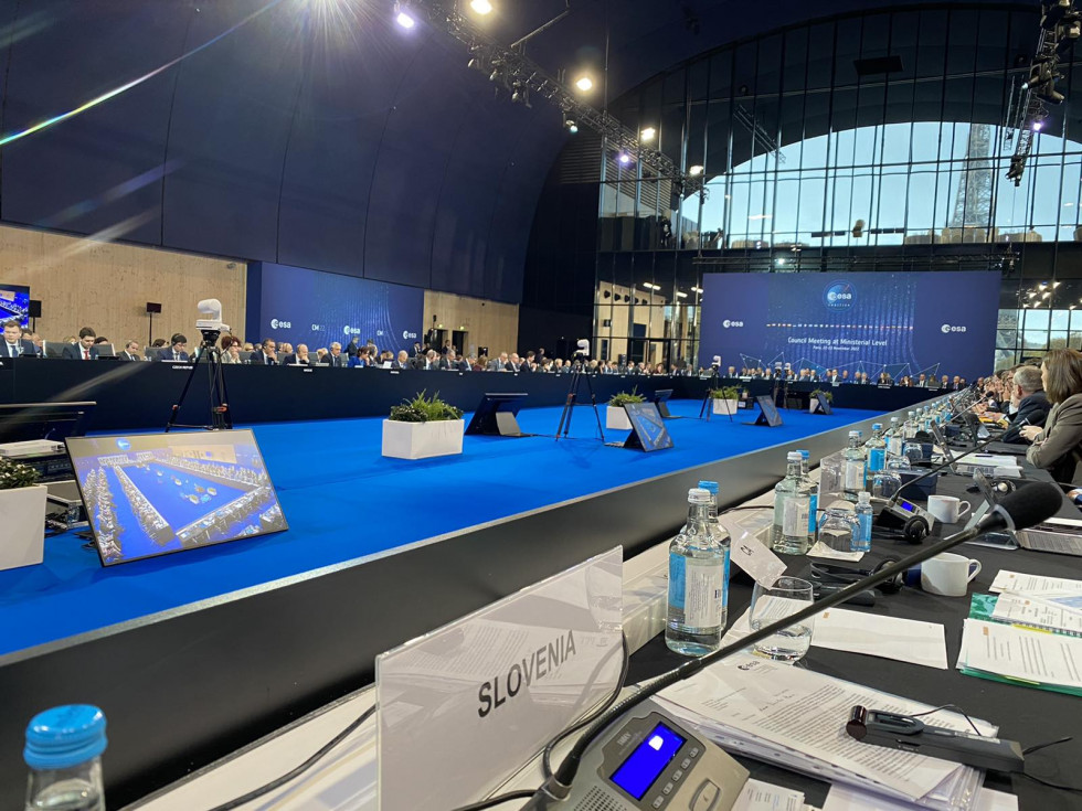 A table with a plaque with Slovenia on it and a big blue hall in the background