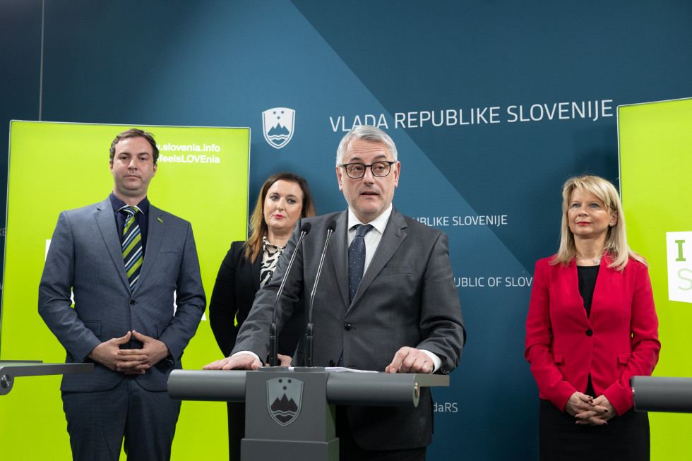 Štiri osebe (Matjaž Han, Maja Pak, Rok Capl, Petra Bezjak Cirman), za njimi platno z logotipi vlade v ospredju minister za govornico