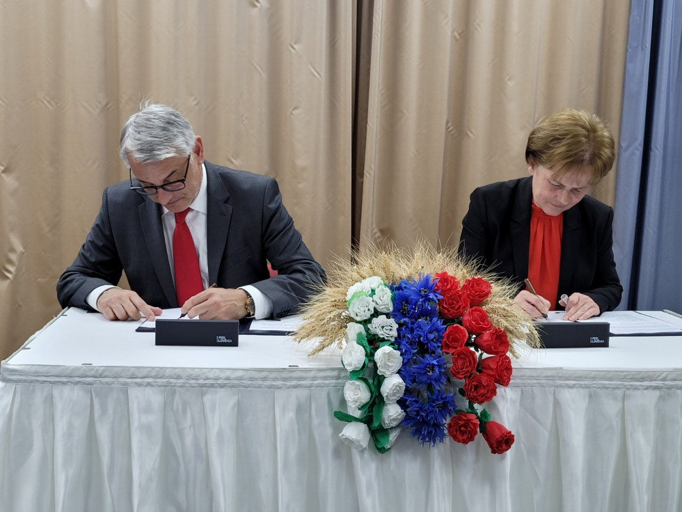 Minister Han in Andrea Kovacs za mizo s cvetjem podpisujeta pogodbo