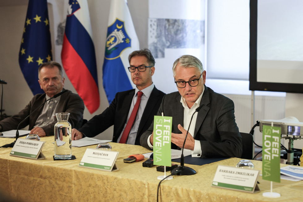 Minister Matjaž Han s še dvema sogovornikoma sedi za mizo med potekom novinarske konference. 