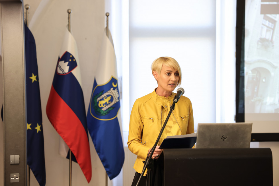 Podžupanja Občine Kamnik Romana Učakar stoji za govorniškim pultom za njo so zastave.