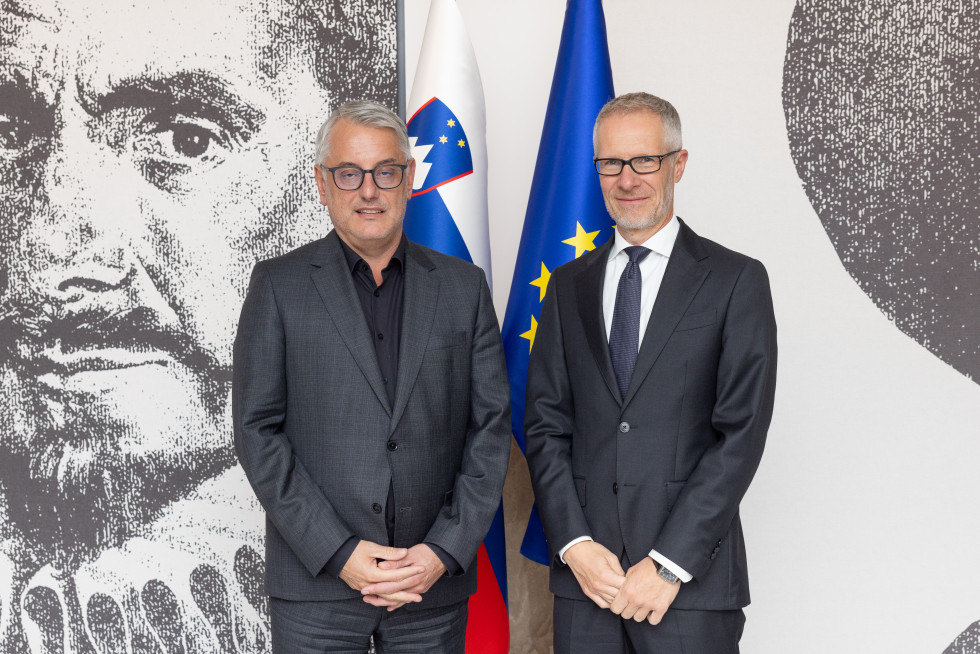 Minister Matjaž Han in guverner Banke Slovenije Boštjan Vasle stojita pred zastavami.