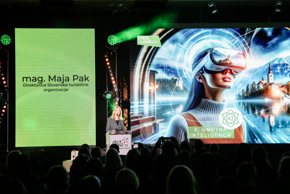 Maja Pak med nastopom, na zaslonu futuristična fotografija ženske z očali, ki omogočajo vpogled v virtualno resničnost