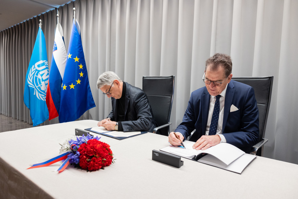 minister in generalni direktor med podpisovanjem sporazuma, v ozadju zastave Republike Slovenije, UNIDO in EU