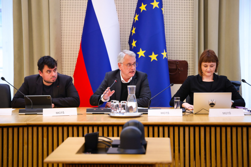 Minister Han za sejno mizo in ob njem dva strokovna sodelavca. Zadaj slovenska in evropska zastava.