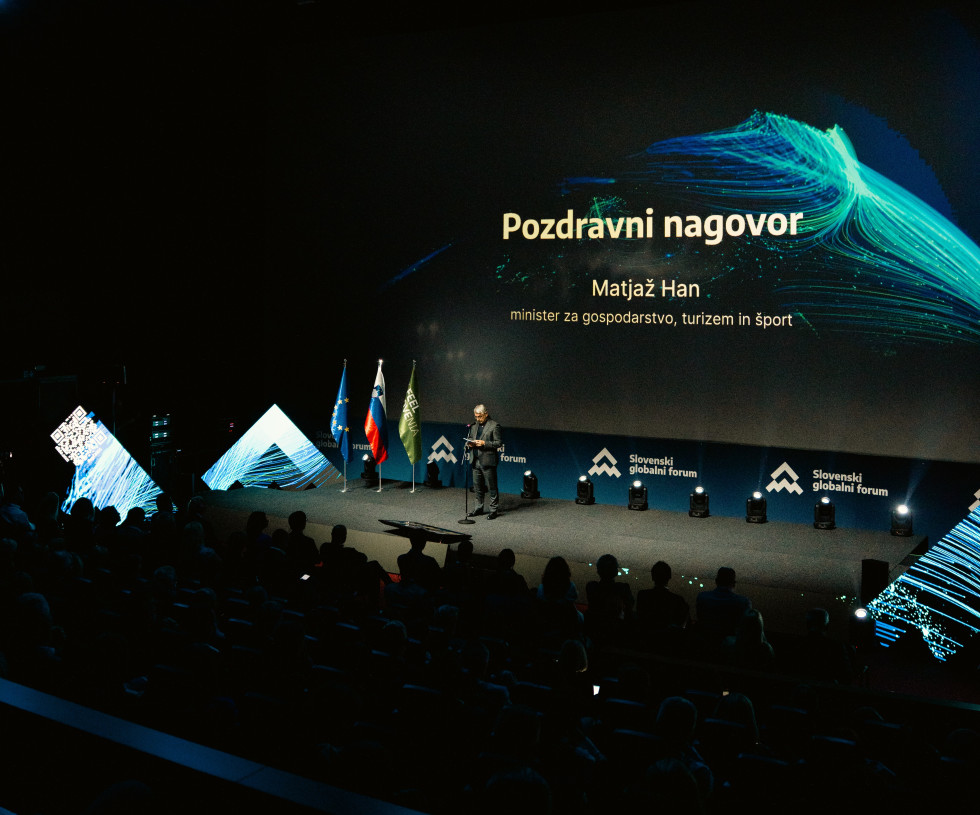 Minister Matjaž Han med govorom na odru. Zadaj velik zaslon s predstavitvijo.