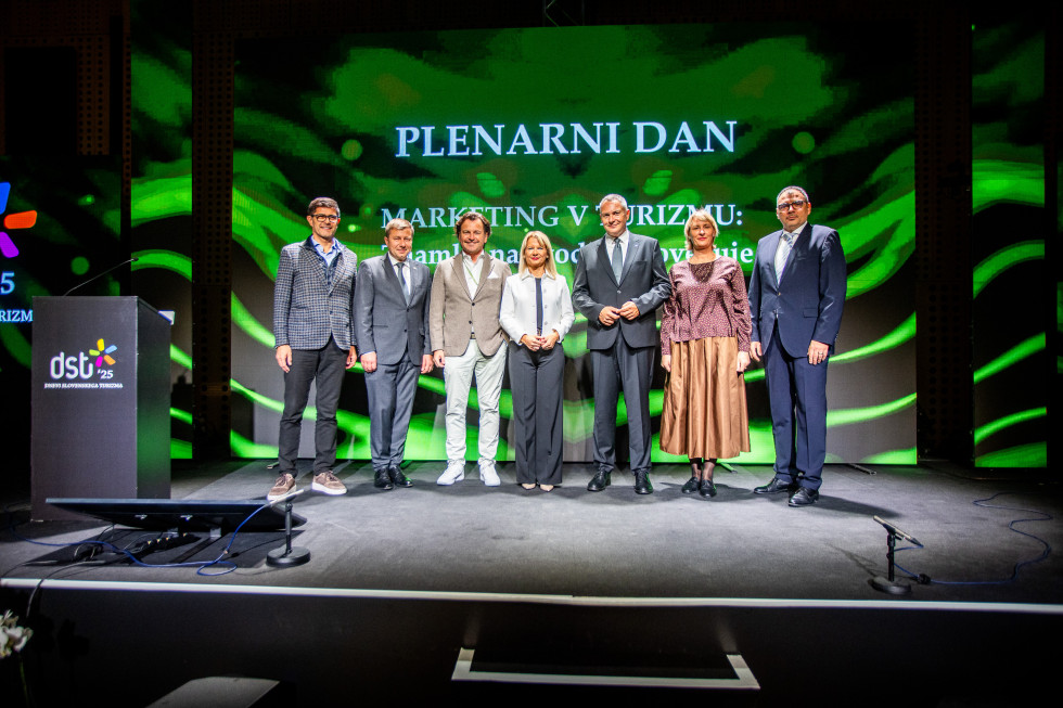 Nagrajenci stojijo na odru. Zadaj veliko zeleno ozadje in napis Plenarni dan.